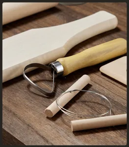 Detailed view of pottery clay sculpting tools including loop tool and wire cutter on wood.