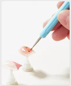 Detail shot of the nail dotting pen featuring a blue handle and fine metal tip for nail art.