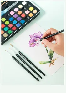Nahaufnahme von Feinkunst-Malpinseln mit schwarzen Griffen und Aquarellfarben-Set auf dem Tisch.