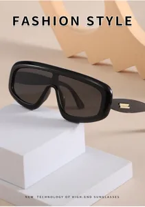 Occhiali da sole scuri futuristici con montatura spessa e dettaglio metallico dorato.
