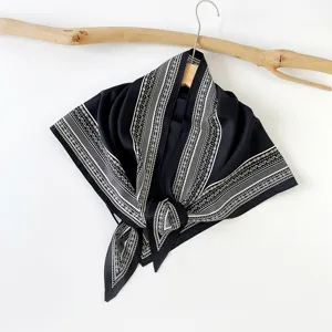 Detailansicht eines schwarz-weißen Paisleymuster-Seidenschals elegant auf Holz.