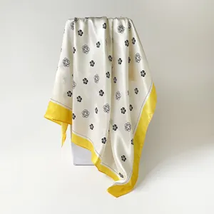 Detail shot of 90cm satin square silk scarf featuring chic floral print and vibrant yellow border.
