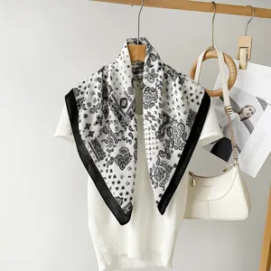 Detailed view of black and white paisley print square scarf styled on white top with chic prop.