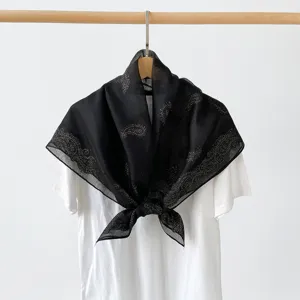 Detailed view of elegant black square scarf featuring gold paisley pattern displayed nicely.