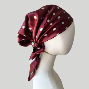 Close-up detail of the burgundy satin polka dot headscarf cap, showing smooth texture and drapes.