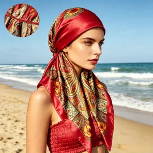 Detailed close-up of a red satin paisley print headscarf worn by a model on a sunny beach.