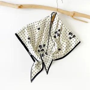 Close-up view of a chic polka dot floral triangular silk scarf featuring elegant black and white design.