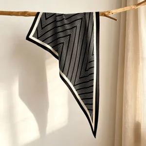 Detailed view of the elegant black and white striped triangle silk scarf draped on a wooden branch.
