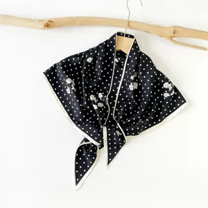 Detailed shot of a black and white polka dot triangular scarf hanging on a rustic wooden hanger.