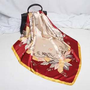 Detail view of a luxury satin square scarf with elegant floral and shell print in red and beige.