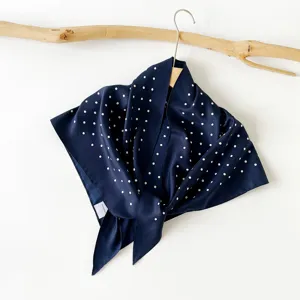 Navy blue silk scarf detail shot, elegant white polka dot pattern on lightweight fabric.