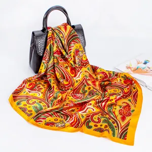 Detailed view of a vibrant yellow paisley print silk satin square scarf draped on a chic handbag.