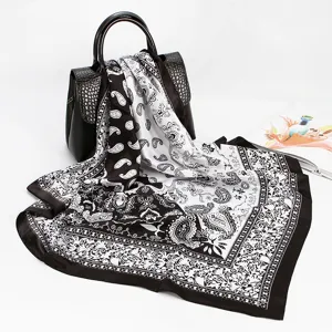 Detailed view of black and white paisley silk scarf draped on leather bag, elegant texture.