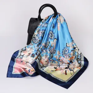 Detailed view of a blue floral satin silk square scarf draped on a black bag prop.