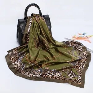 Detailed view of a green silk-feel square scarf with leopard chain print draped on black bag.