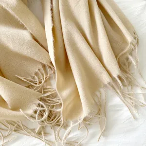 Close-up detail of soft beige cashmere-feel fringed scarf winter warm shawl texture view.