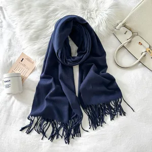 Detailed view of a soft navy blue winter scarf with fringe accents on cozy white blanket.