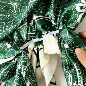 Green satin paisley print bonnet cap detail view showing elastic band and soft inner lining.