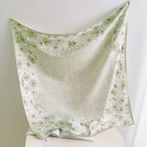 Close-up detail view of the green floral print square scarf draped elegantly on the table.