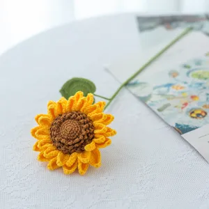 Detailopname van een handgehaakte zonnebloem, met fijne wollen bloemblaadjes en groene steel.