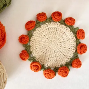 Handmade crochet round coaster with orange roses and green leaves for home table decor.