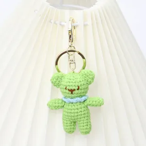 Close-up of the handmade green crochet bear pendant detail, showing fine knitting and metal ring.