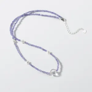 Primo piano dettaglio della collana di perle viola con perle bianche e ciondolo cristallo.