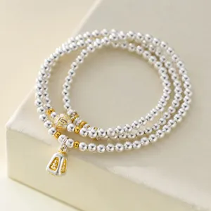 Close-up detail of triple-layer silver beaded bracelet with gold accents and pendant.