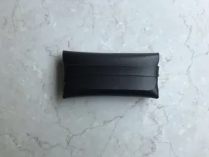 Detailansicht eines eleganten schwarzen Leder-Brillenetuis mit Riemen auf Marmor.