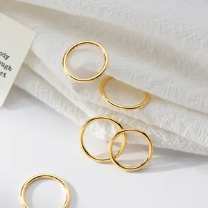 Detail close-up view of minimalist gold-plated silver plain round rings on white fabric.