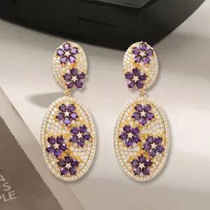 Detaillierte Ansicht luxuriöser goldfarbener Ohrringe mit violetten Blumen und Kristallen.
