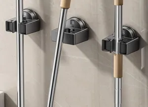 Detailed view of wall-mounted mop and broom holder in dark grey finish for bathroom storage.