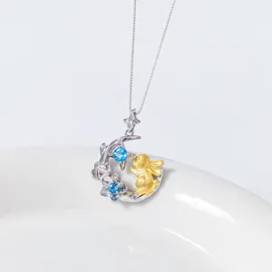Gros plan d'un pendentif lune lapin en argent avec topaze bleue et accent doré design.
