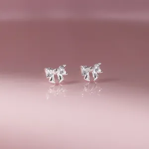 Primo piano di orecchini a lobo con fiocco in argento scintillante su sfondo rosa riflettente.