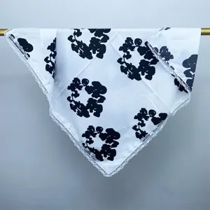 Close-up detail view of elegant white silk scarf with stunning black floral print and lace.