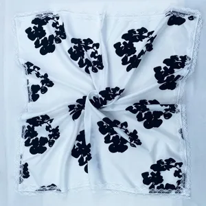 Silk square scarf with black floral print and white lace trim, elegant and versatile accessory.
