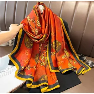 Detailansicht des orangen Seidenschals mit Blumenmuster und dunklem Rand für elegantes Styling.
