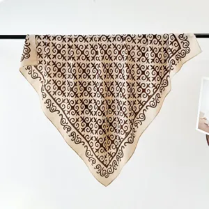 Detailed view of a luxury beige square scarf featuring elegant brown pattern hanging indoors.