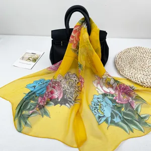 Nahaufnahme eines leuchtend gelben Chiffonschals mit Blumenmuster, elegant über einer Tasche.