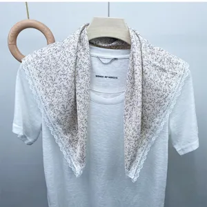 Detail view of floral printed square scarf with delicate white lace trim hanging on display.