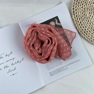 Detailed view of pink polka dot chiffon scarf, elegant rolled rose shape flat lay setup.