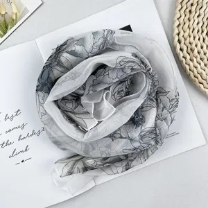 Detailansicht eines eleganten grau-weißen Schals mit Blumenmuster aus Chiffon, kunstvoll gerollt.
