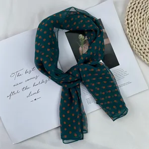 Detail shot of retro dark green chiffon scarf with orange polka dots, lightweight sun protection.