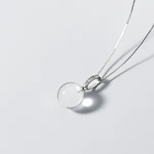 Gros plan d'un pendentif boule en cristal transparent avec chaîne en argent, épuré.