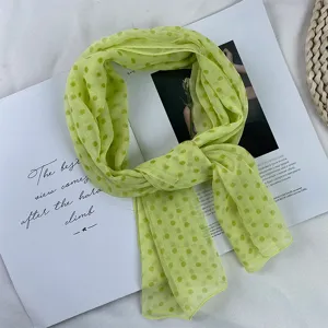 Close-up detail shot of light green polka dot georgette scarf on open magazine background.