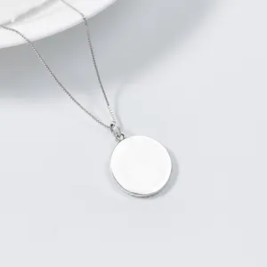 Detailed shot of a minimalist silver round disc pendant necklace on a clean white tray.