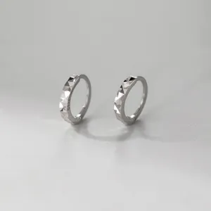 Close-up detail of S925 sterling silver geometric faceted hoop earrings, delicate carved design.
