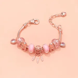 Detalle de pulsera de dijes de oro rosa, con cuentas de vidrio rosa y osito atrapasueños.