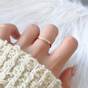 Close-up detail of dainty red cord ring with small silver beads on soft knit texture.