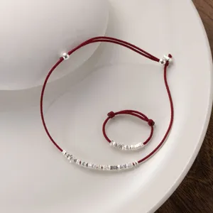 Detail shot of delicate silver fragment red rope bracelet and ring set, minimalist Chinese style.